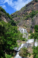 Waterfall cascades down rugged rocky cliffs surrounded by lush green forest in the highlands of Nuwara Eliya, Sri Lanka © nilanka