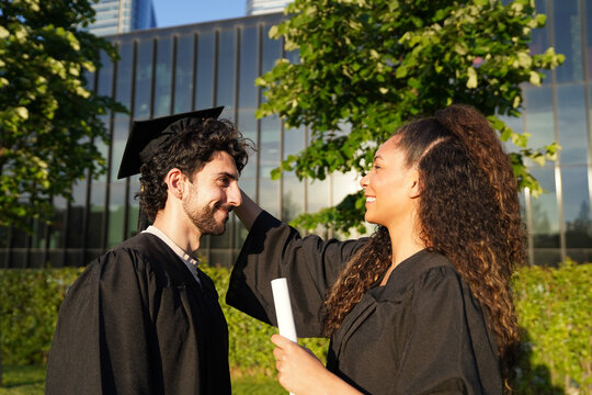 Graduates in caps and gowns celebrate outdoors, sharing joyful moments as a multiracial couple smiles together