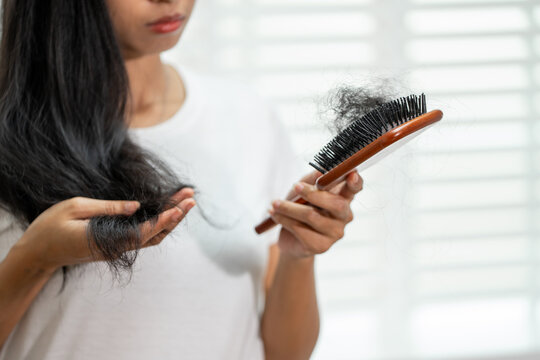 Woman holding a hairbrush with fallen hair while checking hair loss at home