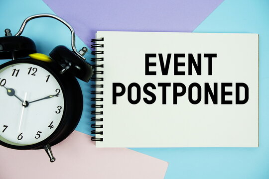 Event Postponed text written on notepad with alarm clock flat lay on multicolor pastel background