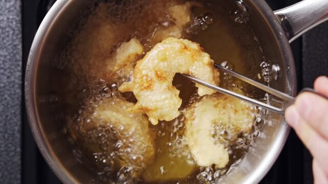Tweezers lift shrimp from hot oil during deep frying. Deep frying uses long tools, dry hands and stable cookware to reduce splashes. Deep frying cooks shrimp, fish, chicken, potatoes or vegetables.