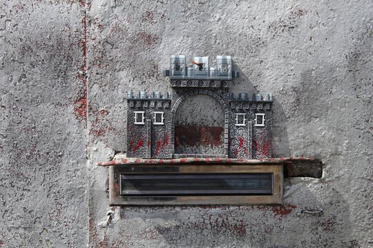 Original metal mailbox in the shape of a castle, with an aged look, mounted on a city wall