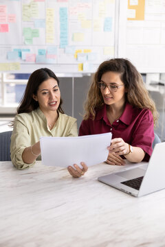 Businesswomen reviewing document at corporate office desk, analyzing report, comparing data, discussing project detail, checking information. Business planning, professional collaboration in workplace