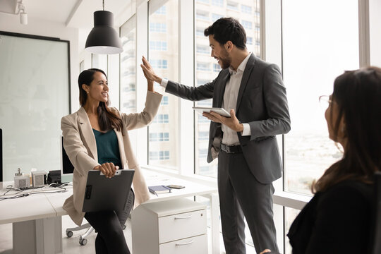 Smiling business team members giving high five, celebrate shared professional success, achieving corporate goal, finish effective collaborative workflow in coworking office. Teamwork, result, unity