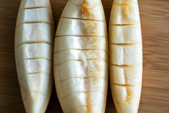 Three freshly cut slices of juicy yellow melon placed on a round wooden chopping board. The melon pulp is sliced into convenient bite-sized pieces, highlighting its soft texture. 