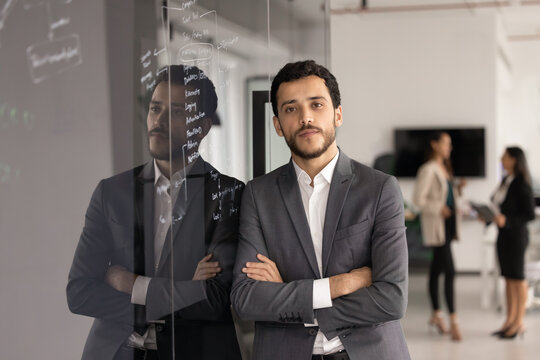 Portrait of confident businessman, team members stand with arms-crossed in corporate coworking office near glass board with strategy notes, representing leadership, decision-making, project planning