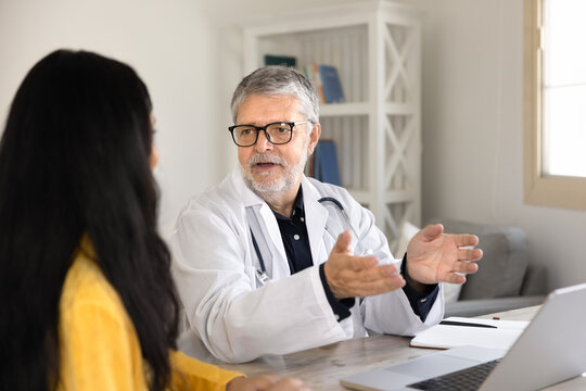 Senior male doctor consulting woman patient, explaining diagnosis or treatment plan, giving health advices and recommendations at clinic desk. Healthcare consultation, professional medical services