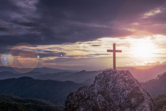 Silhouettes of crucifix symbol on top mountain with bright sunbeam on the colorful sky background