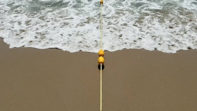 Overhead View of Safety Buoy Rope on the sand in Foamy sea waves. Swimming Hotel Beach Zone concept