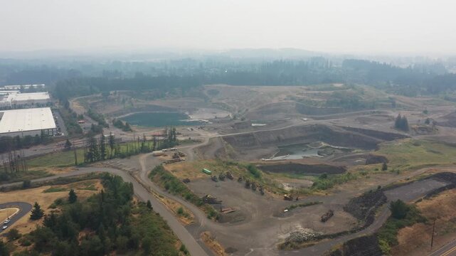 4K aerial drone footage of an active aggregate quarry in Sherwood, Oregon, USA under heavy wildfire smoke and hazy skies. Large open pit mine extracting rock and gravel amid poor air quality condition