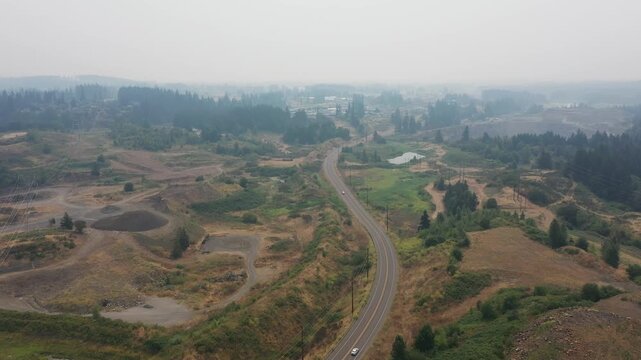 4K aerial drone footage of road through active aggregate quarry near Sherwood, Oregon, USA under heavy smoke from active summer wildfires, highlighting poor air quality, haze and industrial landscape