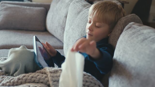Sick boy blowing his nose watching tablet on sofa