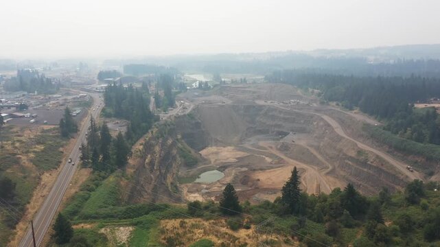 4K aerial drone footage of an active aggregate quarry in Sherwood, Oregon, USA under heavy wildfire smoke and hazy skies. Large open pit mine extracting rock and gravel amid poor air quality condition