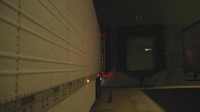 Semi truck backing into warehouse loading dock at night
