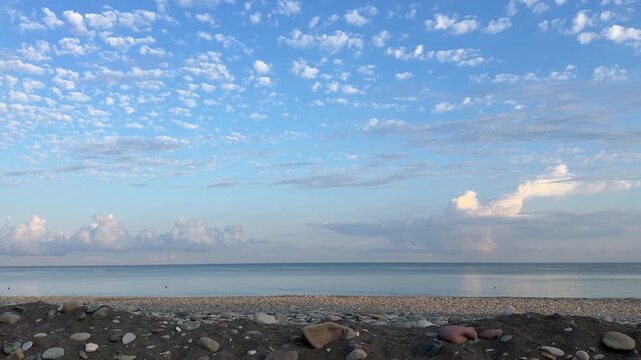 Calm pebble beach under blue sky with fluffy altocumulus clouds at sunrise
