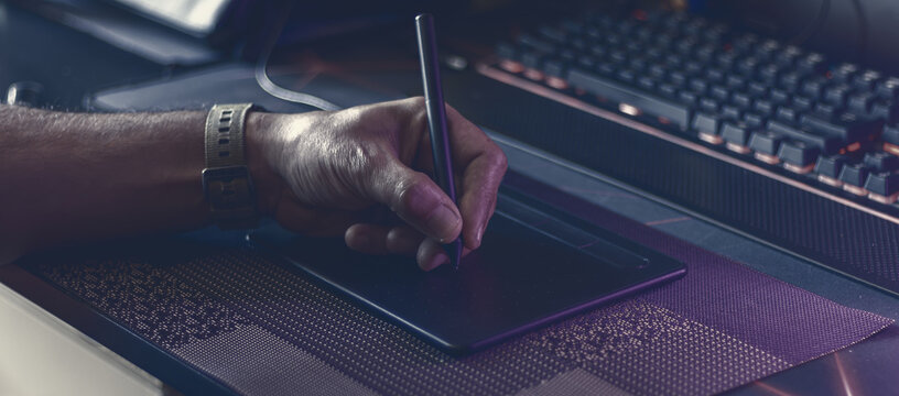 Moody atmospheric shot of a digital artist working on a graphic tablet with a stylus in a studio