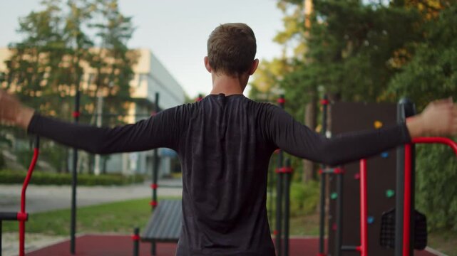 Male athlete performing a dynamic upper body warm up routine before a workout at an outdoor gym. Man warming up shoulders beforea calisthenics training on an outside training ground.
