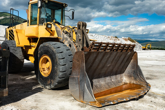 Powerful industrial earthmoving machinery standing idle at a stone extraction facility featuring giant rubber wheels and heavy steel loader bucket for mining raw white marble materials efficiently.
