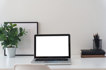 Fototapeta premium Minimal home office workspace with laptop mockup, headphones, coffee cup, notebooks, pencils, and small plant on a clean white desk.
