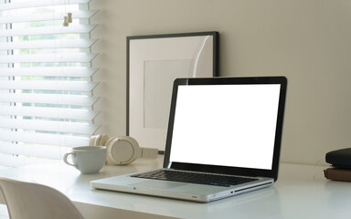 Naklejka premium Minimal home office workspace with laptop mockup, headphones, coffee cup, notebooks, pencils, and small plant on a clean white desk.