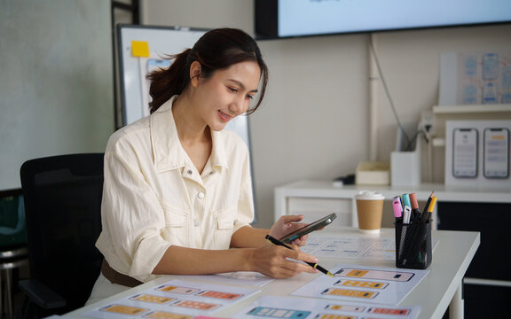 Female UX designer working on mobile app wireframes and interface layouts with sticky notes during a creative design process in a modern office.