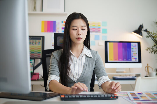 Female graphic designer working on a desktop computer in a modern creative office with colorful design references.