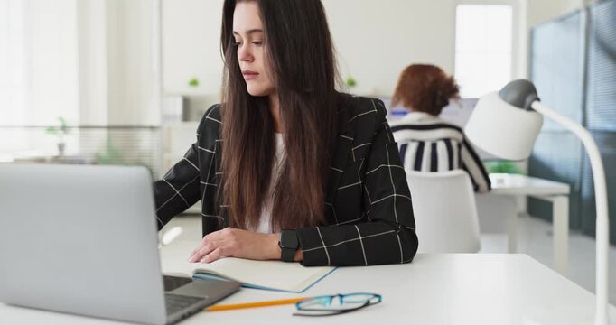 Businesswoman with laptop in office working. She refines goals and organizes tasks at a tidy desk, showing focus, strategy, and a modern corporate setting. Clear concept of planning focus.