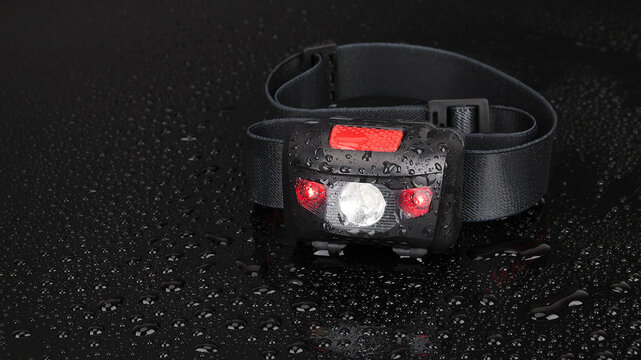 Waterproof LED headlamp on wet black surface for camping and hiking