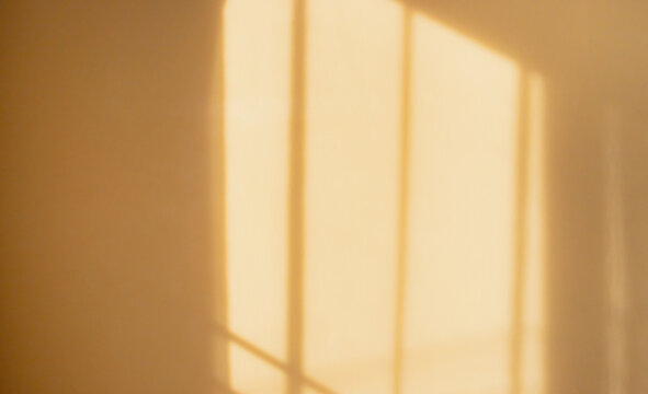 Warm sunlight casting soft window shadows on a beige wall. Creating a minimalist abstract background with natural light, texture and copy space.
