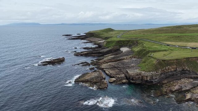 Cinematic drone view of Mullaghmore Head, County Sligo, northwest Ireland. The smooth flight captures the charming waves crashing against the rocky coast, beautiful horizon with dramatic cloudy sky.