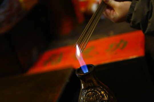 A person lights incense sticks with a gas burner in a temple.