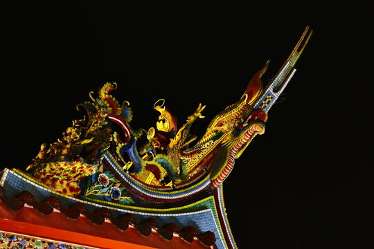 Intricate dragon sculpture on a traditional Taiwanese temple roof at night.