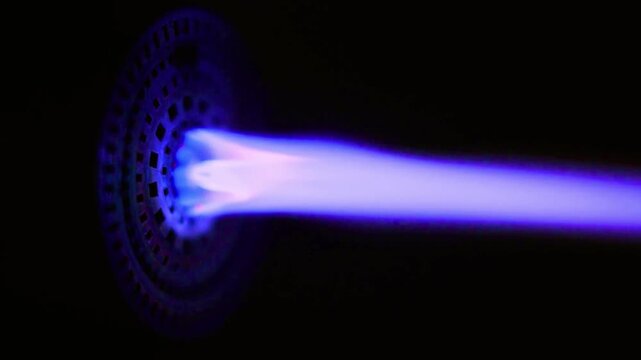 Industrial gas burner nozzle firing blue flames in dark laboratory space
