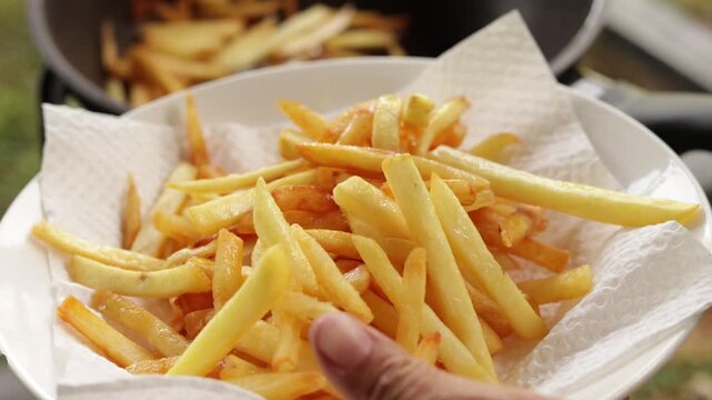 Close-up of freshly fried golden French fries being transferred with a strainer spoon onto a paper towel-lined plate. Action video footage showing fast food cooking, preparation, and crispy snack.
