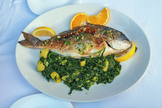 Balkan cuisine. Grilled fish of  sea bream with green leafy vegetables on white plate
