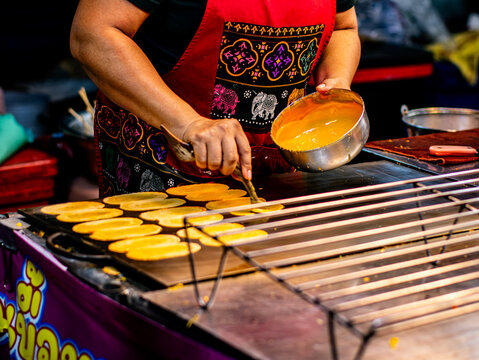 Thai Street Vendor Pouring Coconut Batter to Make Khanom Buang Crispy Pancakes on Hot Griddle