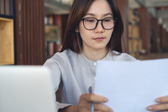 Focused businesswoman reviewing business documents with laptop on table in modern office, workspace, business planning concept.
