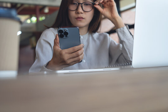 Business woman thinking during using smartphone and working on laptop computer at cafe modern workspace, notebook on desk, online studying or remote work, corporate business concept, close up