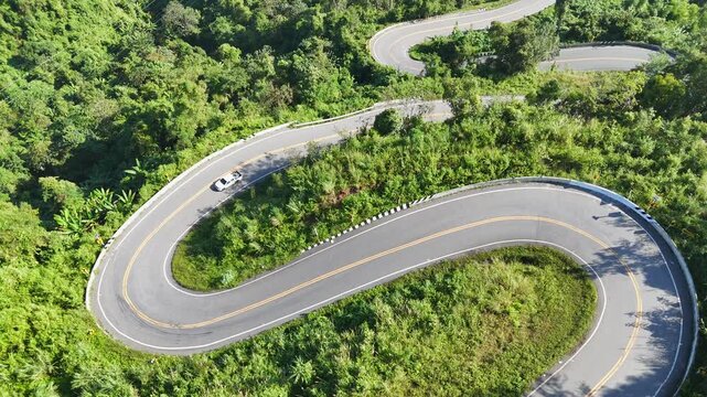 A private car is traveling on a winding road that follows the mountain terrain of Nan province.