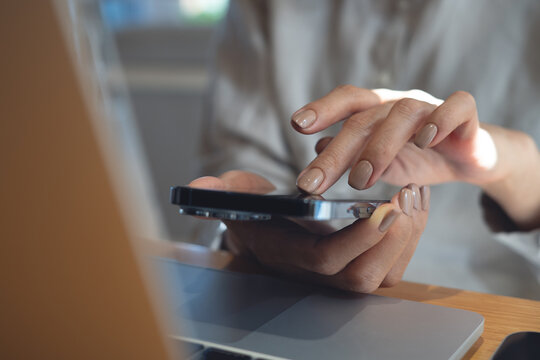 Close-up of woman using smartphone with laptop on table in cafe or modern office, soft natural light. online working remotely, modern business lifestyle