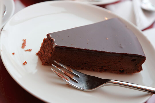 Rich Dark Chocolate Cake Slice with Glossy Ganache and Silver Fork on White Plate