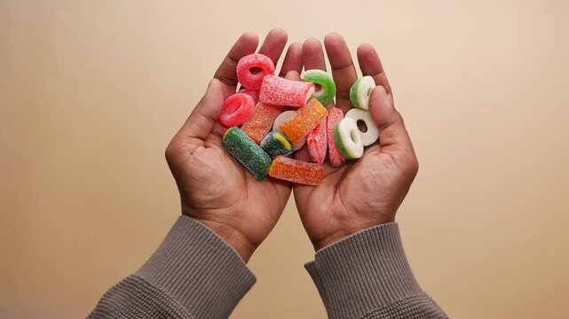 Hands holding colorful candy on plain background