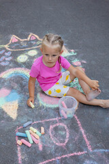 Naklejka premium Little girl draws with colorful chalk on the asphalt on the street in summer