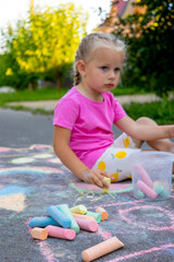 Fototapeta premium Little girl draws with colorful chalk on the asphalt on the street in summer