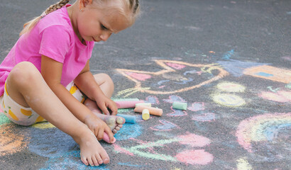 Fototapeta premium Little girl draws with colorful chalk on the asphalt on the street in summer.