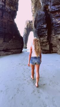 rear view of a young woman walking through natural rock arches on cathedrals beach in galicia spain