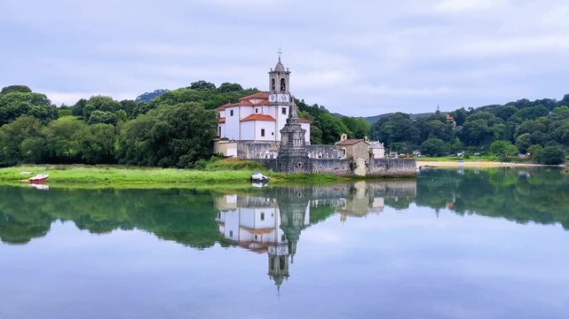 scenic view of a church reflected in a calm river surrounded by green trees. church of nuestra senora de los dolores reflected in ria de niembro llanes asturias spain