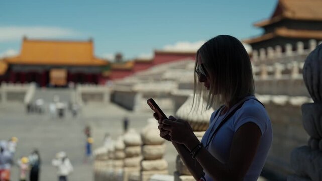 Tourists visiting famous Palace Museum in Beijing, China, woman with smartphone. Female traveler posting and sharing pictures in social media when traveling in Asia, summer trip in asian region