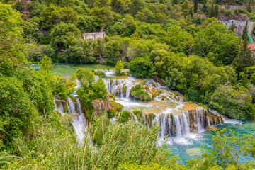 Krka National Park, Croatia, view of the Krka waterfall on a sunny day, featuring cascading water, lush greenery, wooden walkways, and a stunning natural landscape in bright Mediterranean light. © johnkruger1