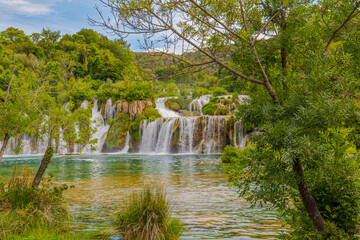 Krka National Park, Croatia, view of the Krka waterfall on a sunny day, featuring cascading water, lush greenery, wooden walkways, and a stunning natural landscape in bright Mediterranean light. © johnkruger1